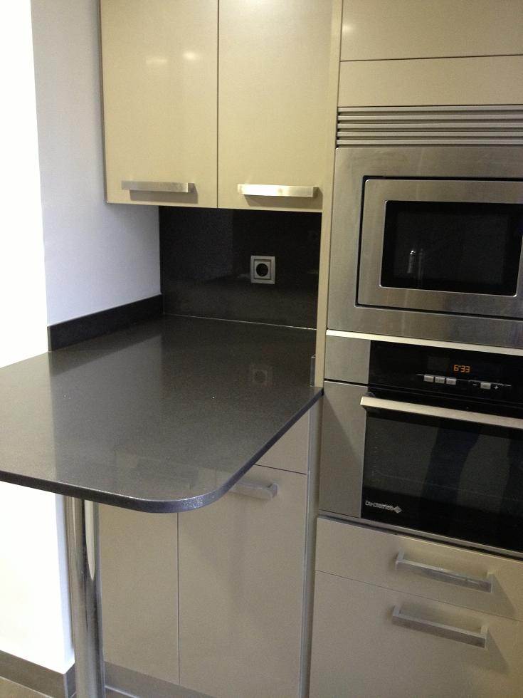 Cocina de diseño en París (Francia) con mobiliario color champán y una pequeña barra de desayuno integrada, optimizando el espacio en una reforma cerca del Arco del Triunfo.