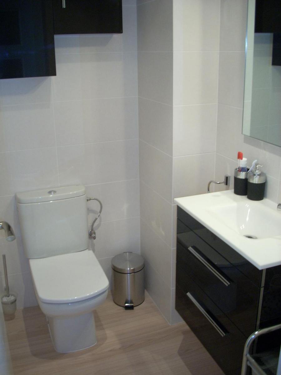 Baño de dimensiones reducidas en Sant Andreu con suelo laminado Quick-Step resistente al agua, inodoro compacto y diseño moderno en Barcelona.