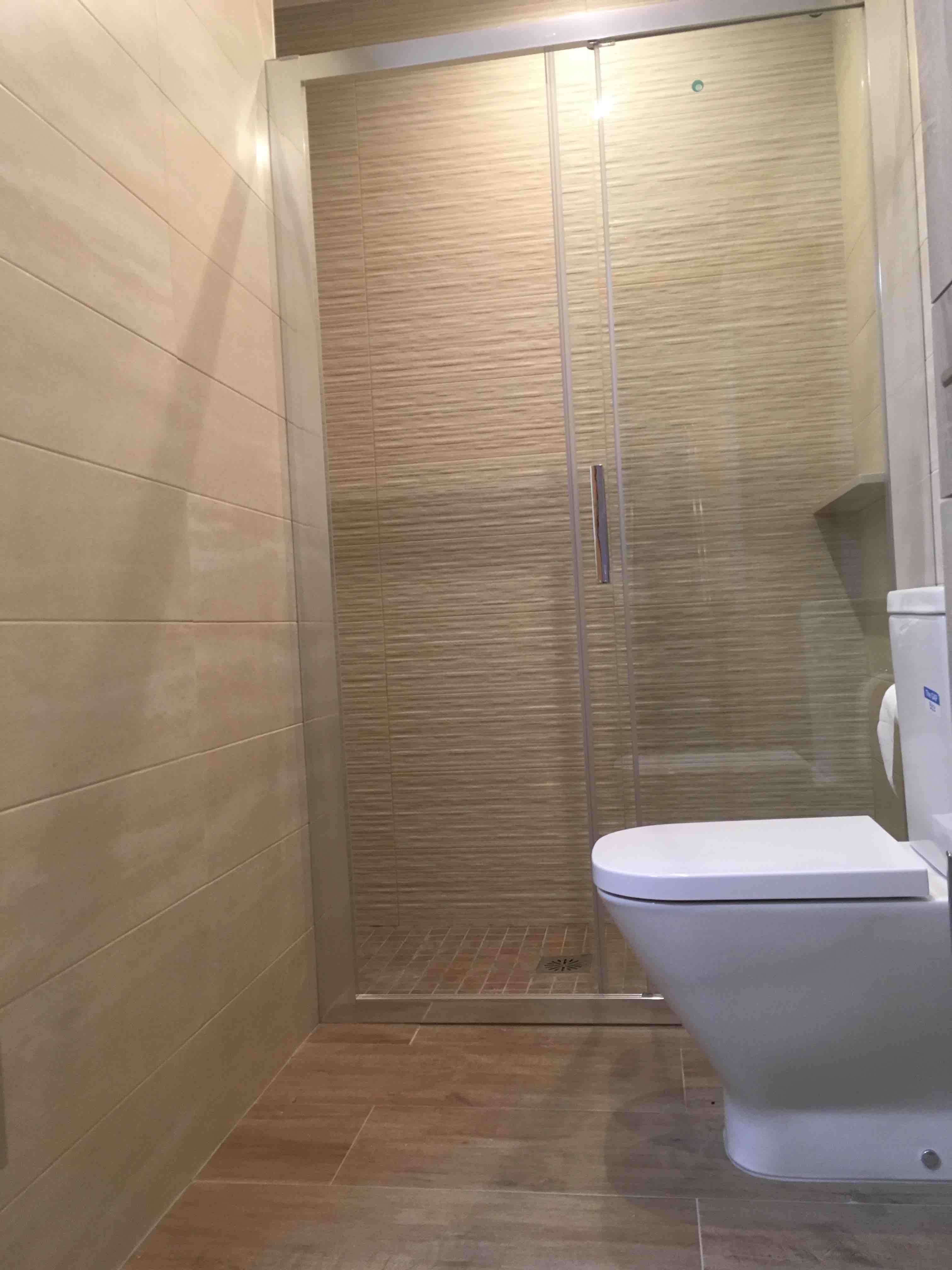 Reforma integral de baño en Sant Boi con plato de ducha de obra y revestimiento cerámico de pared con acabado rugoso.