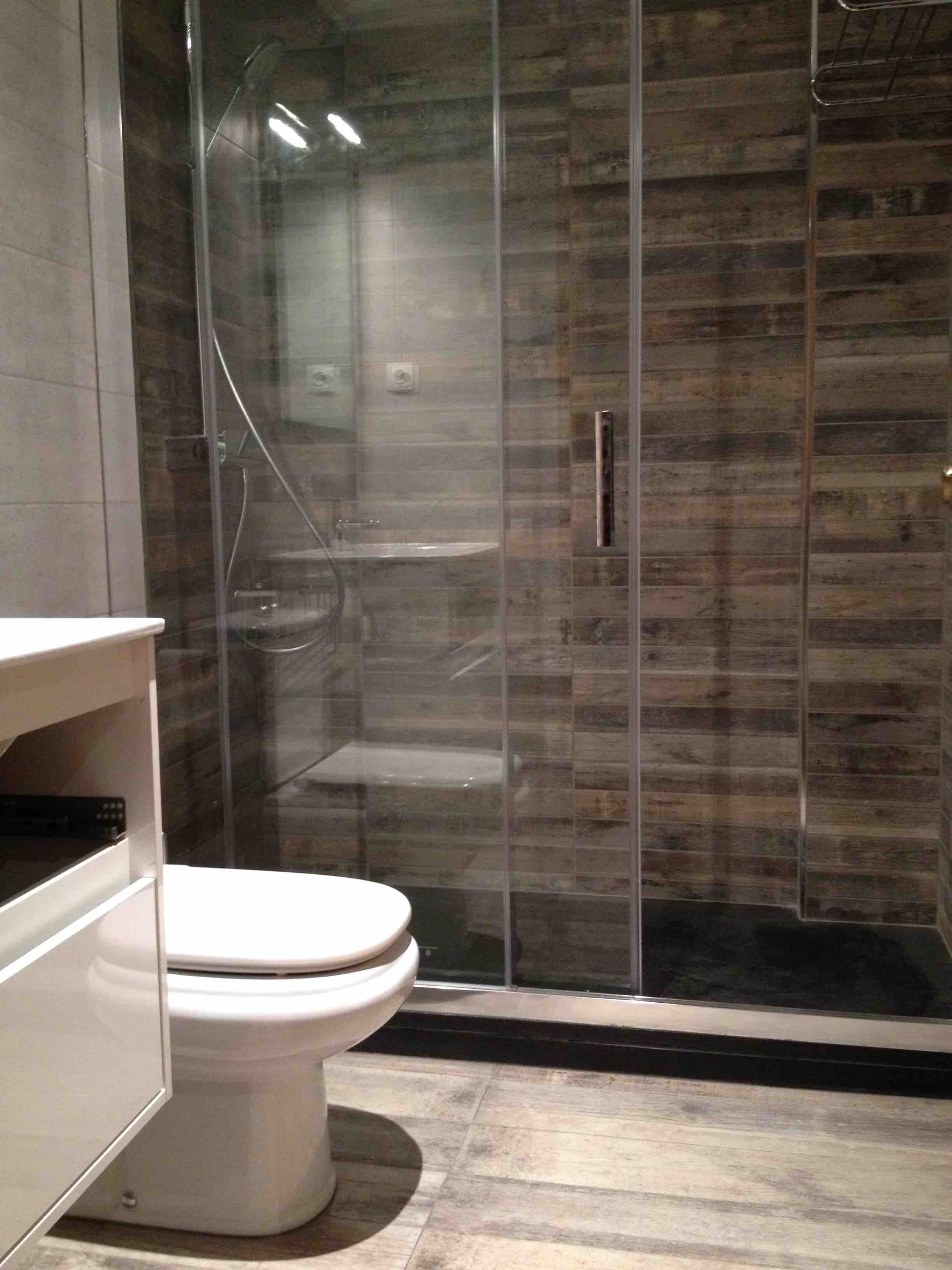 Zona ducha con alicatado oscuro y mampara corredera. Reforma de cuarto de baño en planta baja en Carrer Lopez Catala, en el Barrio de Sants en Barcelona.