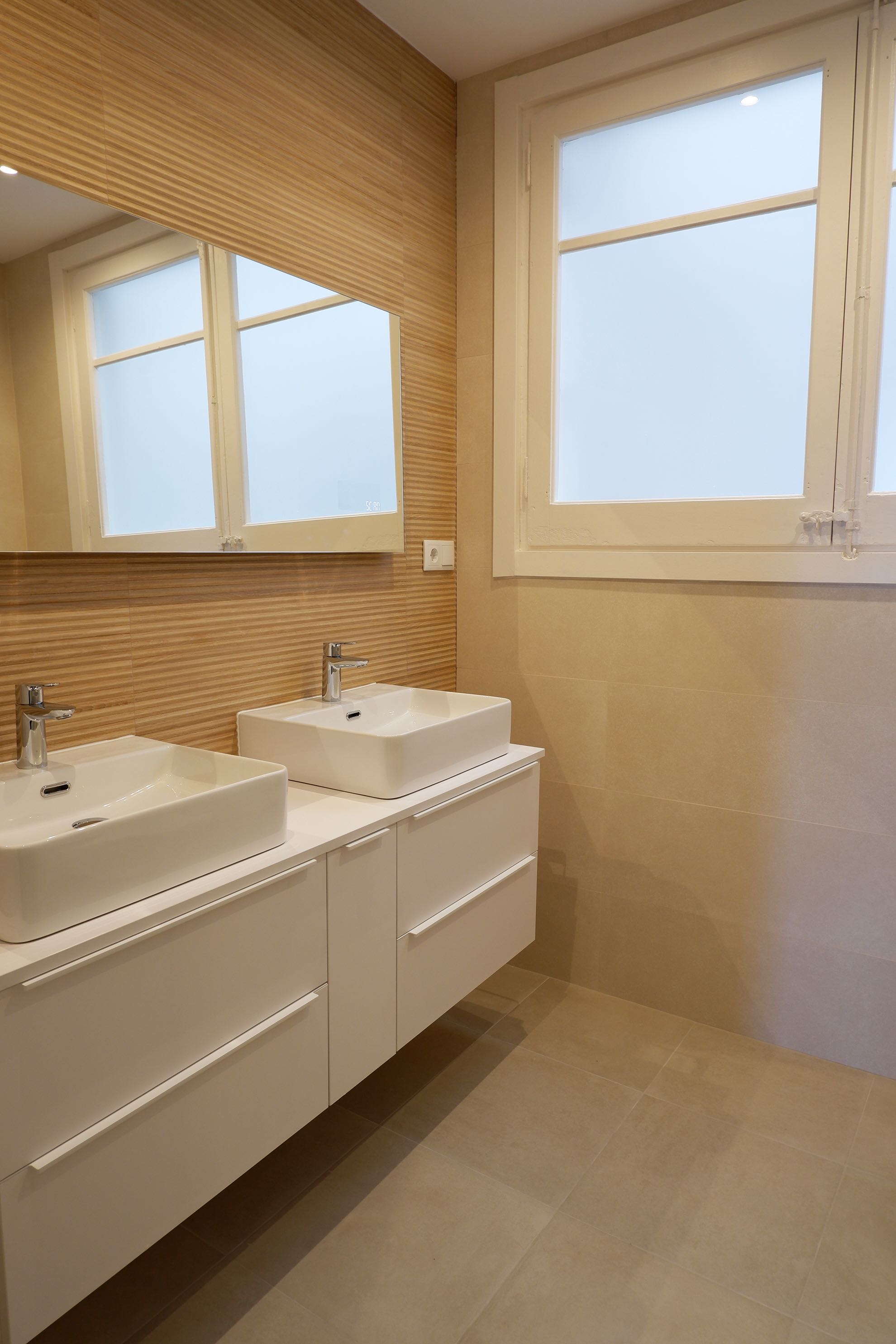 Reforma de baño en l'Eixample con alicatado frontal de imitación madera, mueble de baño doble y dos lavabos sobreencimera en Barcelona.