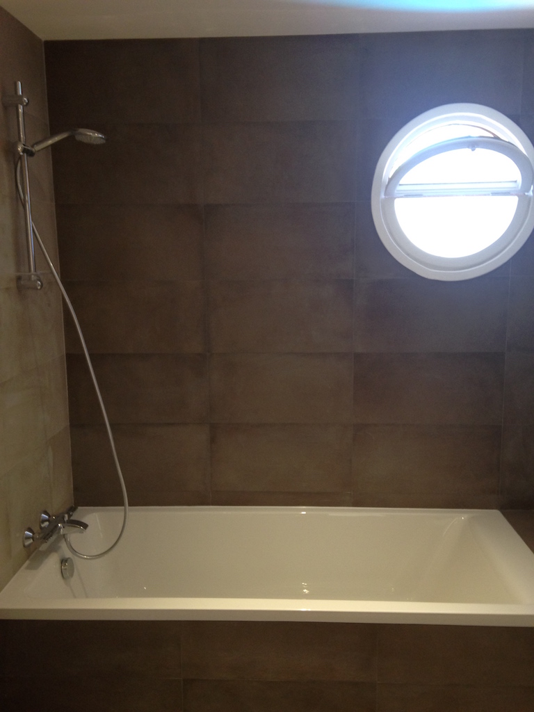 Zona de baño en Sant Just Desvern con bañera encastrada situada bajo una ventana circular de época recuperada, aportando luz natural y vistas.