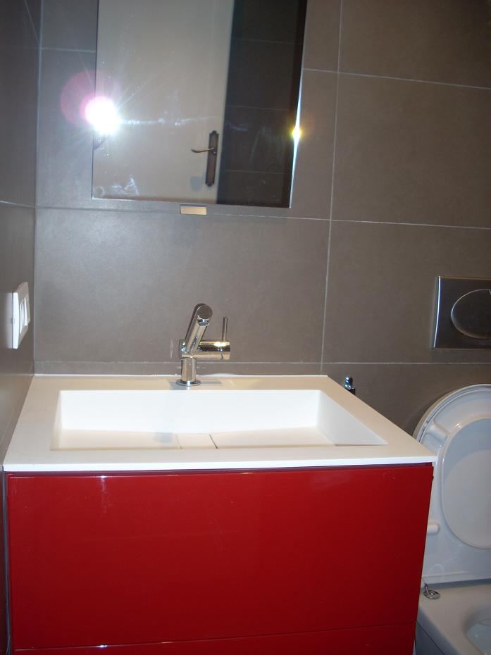 Detalle de baño moderno con mueble de lavabo suspendido en color rojo intenso sobre revestimiento de pared con baldosas cerámicas de gran formato en tonos neutros.
