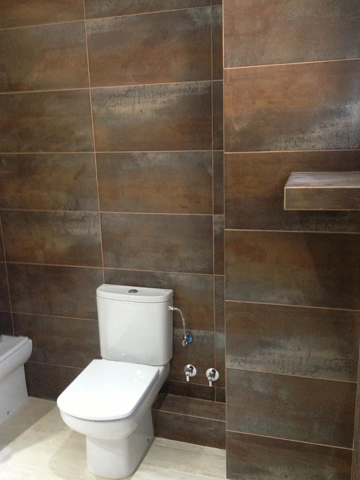 Baño principal en Sant Cugat con paredes revestidas en baldosa cerámica de gran formato con acabado efecto óxido y diseño contemporáneo en una rehabilitación integral.