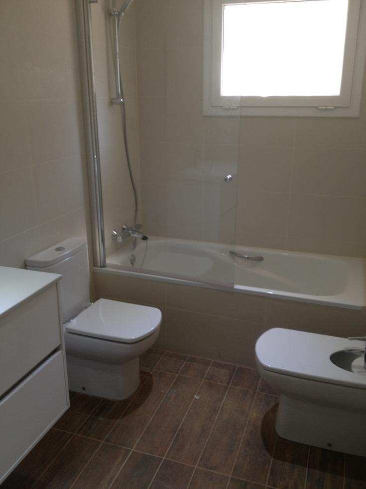 Cuarto de baño en una casa de cuatro plantas en Sant Cugat con bañera acrílica blanca, mampara de cristal templado y revestimiento cerámico en tonos claros.