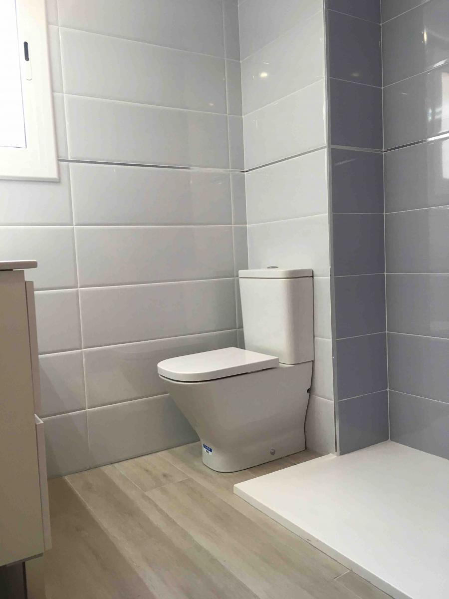Baño  con alicatado  blanco y suelo cerámico imitación madera. Reforma Nou Barris. Barcelona