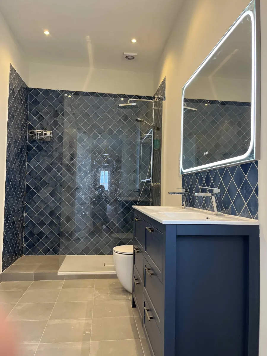 Detalle de plato de ducha con mampara fija de 120cm, junto con mueble en lacado azul y espejo led en zona baño 2. Reforma integral piso en Via Laietana. Gòtic. Barcelona