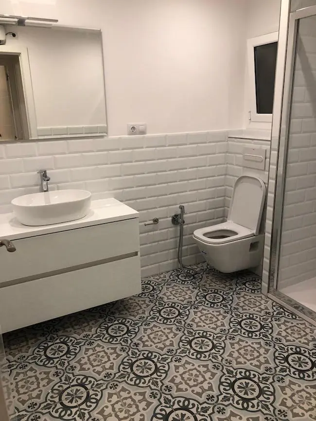 Baño reformado en el barrio de Sants con suelo porcelánico de imitación hidráulico, inodoro suspendido y cisterna empotrada en Barcelona.