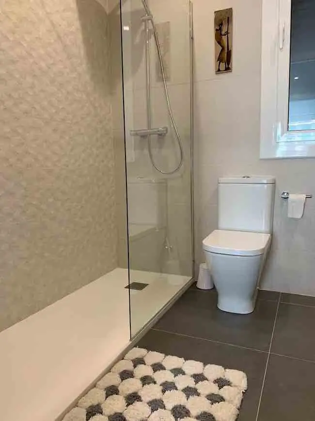 Reforma de baño moderno en el barrio de Sant Antoni con plato de ducha extraplano antideslizante, mampara de cristal fijo con tratamiento antical y acabados neutros en Barcelona.